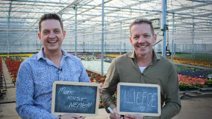 twee mannen in een kas met een krijtbordje in hun handen